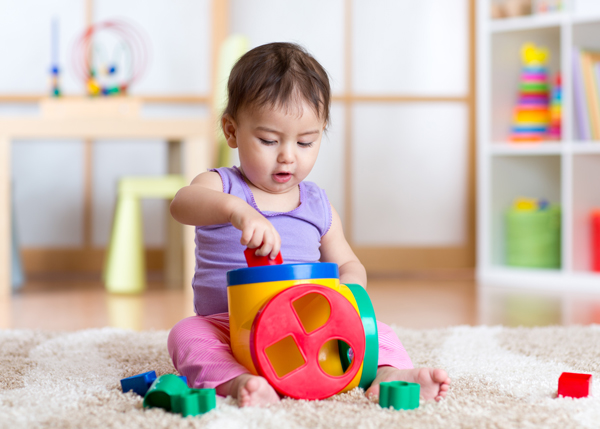 Baby engaging in sensory play for babies using a colourful shape-sorting toy at a nursery, supporting early learning and fine motor development.
